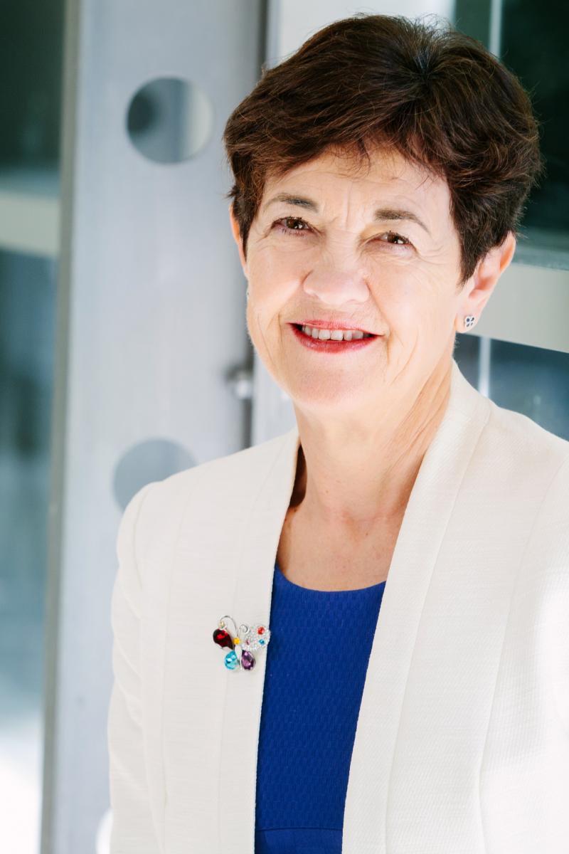 Professor Polly Parker, a white woman with short dark brown hair, is smiling at the camera. She is wearing a royal blue round-neck shirt and a white blazer.